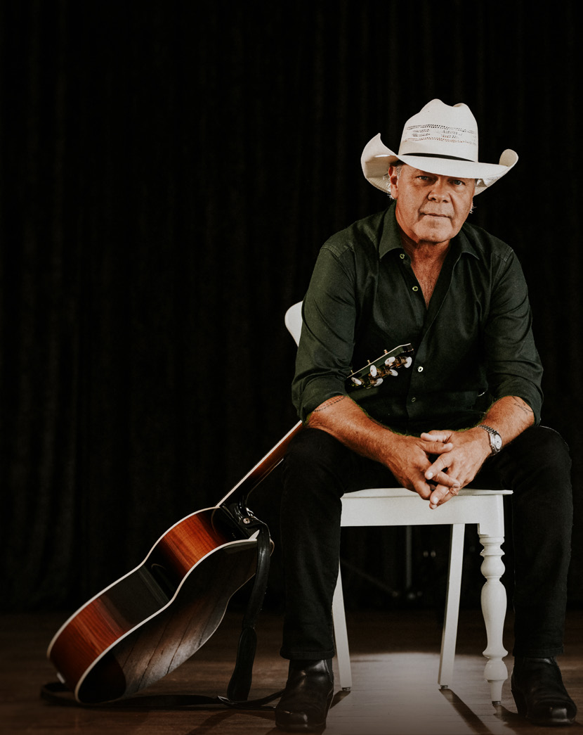 Troy Cassar-Daley in a white hat seated with an acoustic guitar